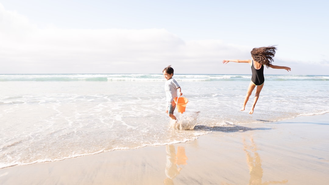 A mother and her children staying kids cool at a sunny Moroccan Atlantic beach, splashing in shallow waves near the shore.