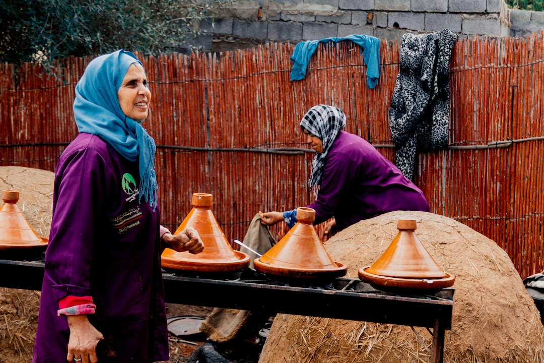 A Moroccan woman lifts the lid of a clay Moroccan tagine at a family table in a traditional riad kitchen.