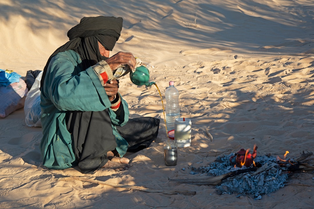 A woman performing the traditional high-pour ritual of Moroccan drinks, serving atay into small glasses in a sunlit courtyard